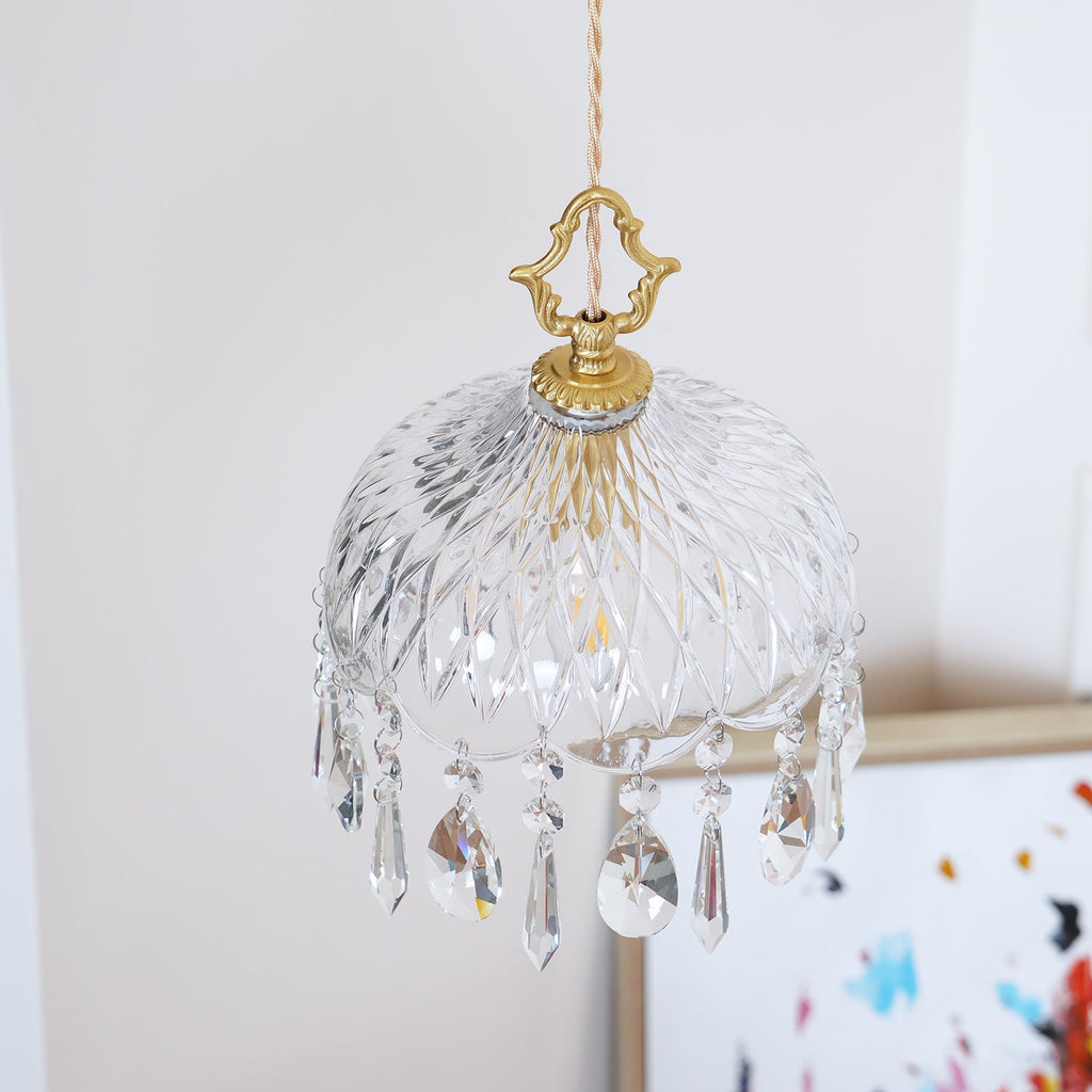 Clérachic crystal-drop pendant lit against a dark patterned glass panel, with crystal drops catching the light.