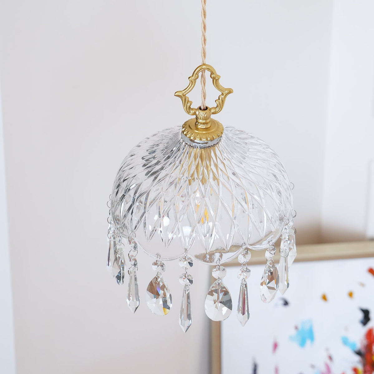 Clérachic crystal-drop pendant lit against a dark patterned glass panel, with crystal drops catching the light.