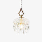 Clérachic crystal-drop pendant on a pale backdrop, with a brass crown finial and a dark twisted cord, with the glass bowl barely lit.