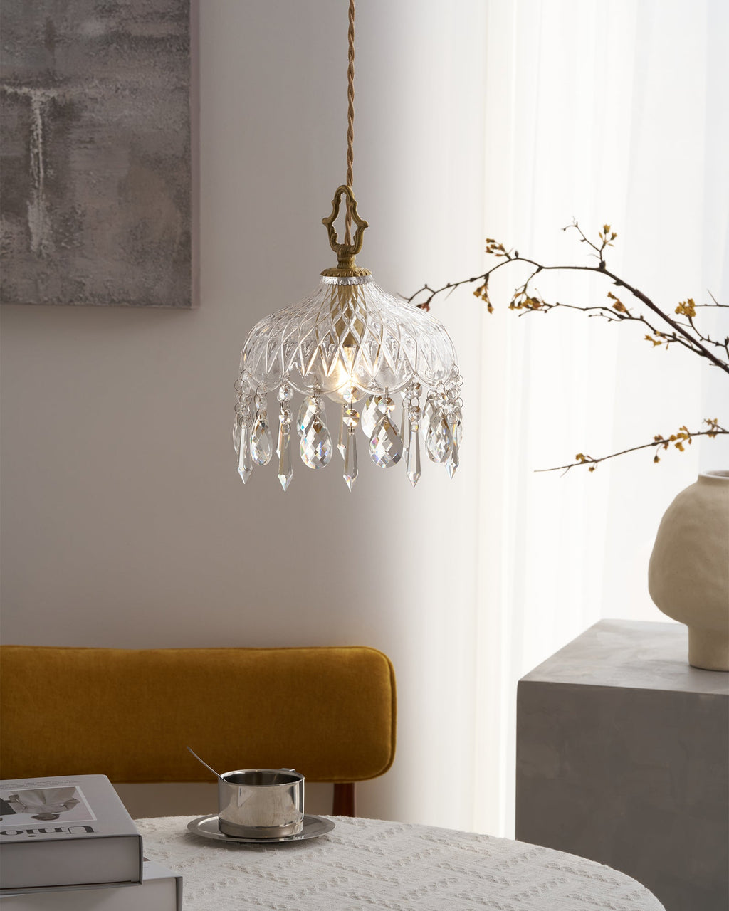 Close view of a lit Clérachic crystal-drop pendant with a diamond-cut glass bowl, beside bare branches and a cream vase.