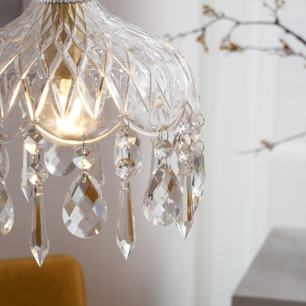 Close view of the diamond-cut glass and the crystal drops on this Clérachic pendant, with the bulb glowing and a branch behind.