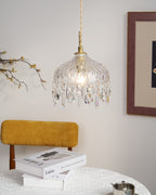 Clérachic crystal-drop pendant lit in a sunlit room, with a mustard chair, stacked books and a framed print with a dark mount.