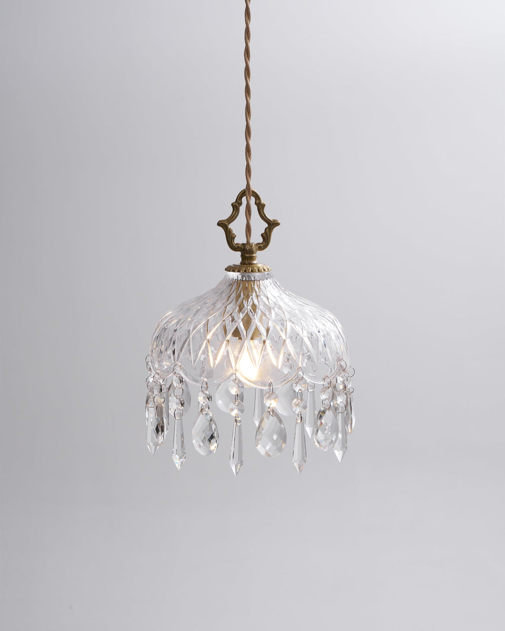 Clérachic cut-glass pendant lit on a plain light grey backdrop, with a brass crown finial and a pale twisted cord.