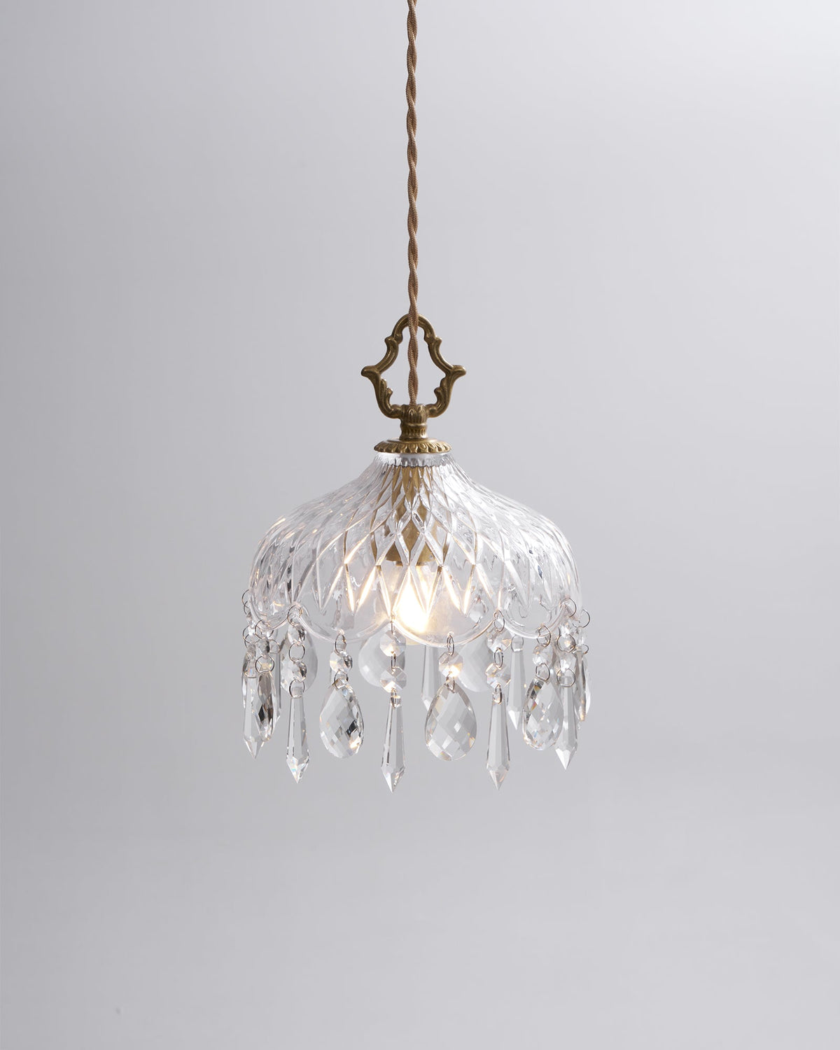Clérachic cut-glass pendant lit on a plain light grey backdrop, with a brass crown finial and a pale twisted cord.