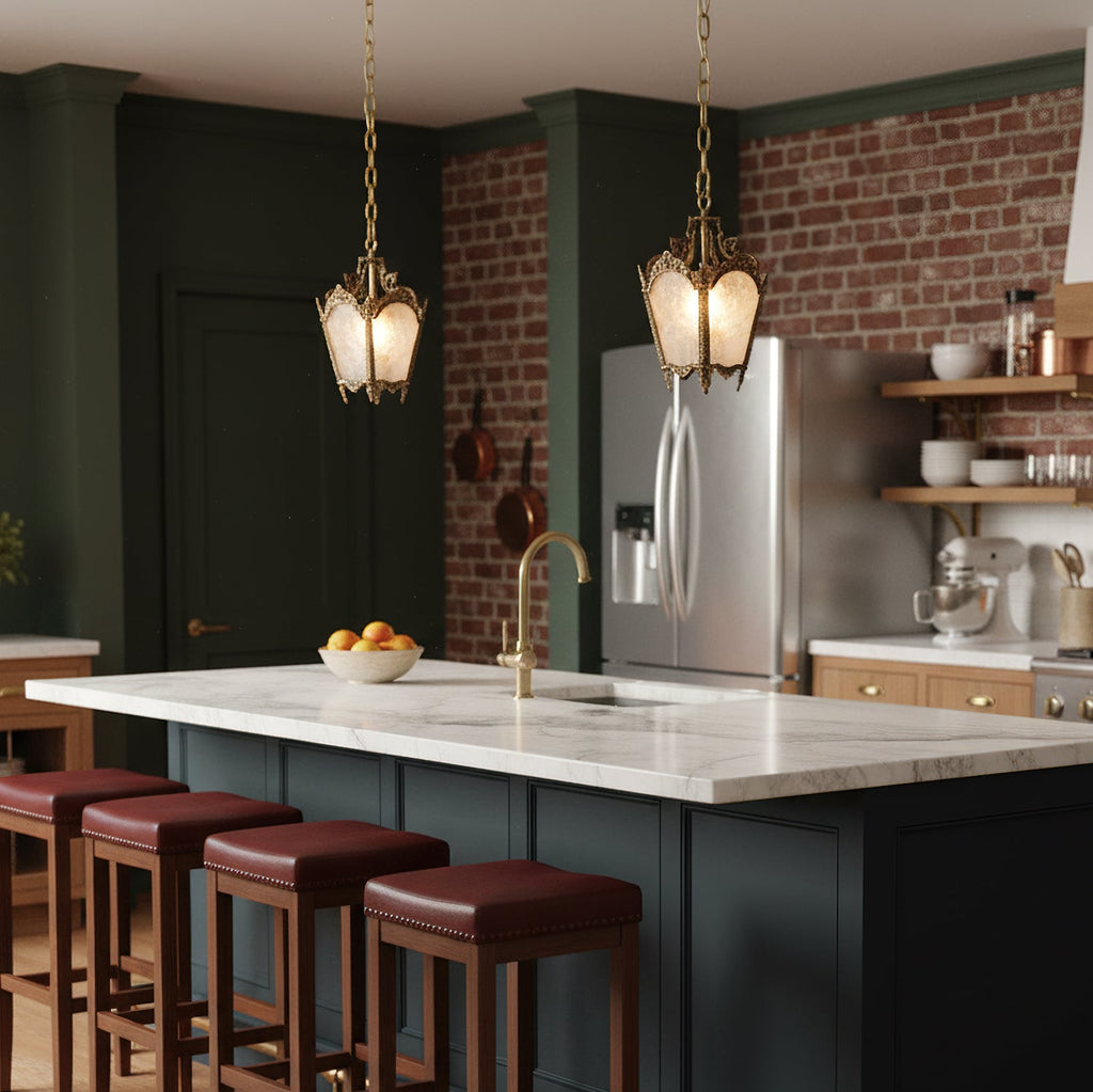 Two small brass Clérachic lantern pendants hang above a marble kitchen island with burgundy bar stools and a dark green wall.