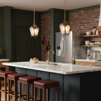 Two small brass Clérachic lantern pendants hang above a marble kitchen island with burgundy bar stools and a dark green wall.
