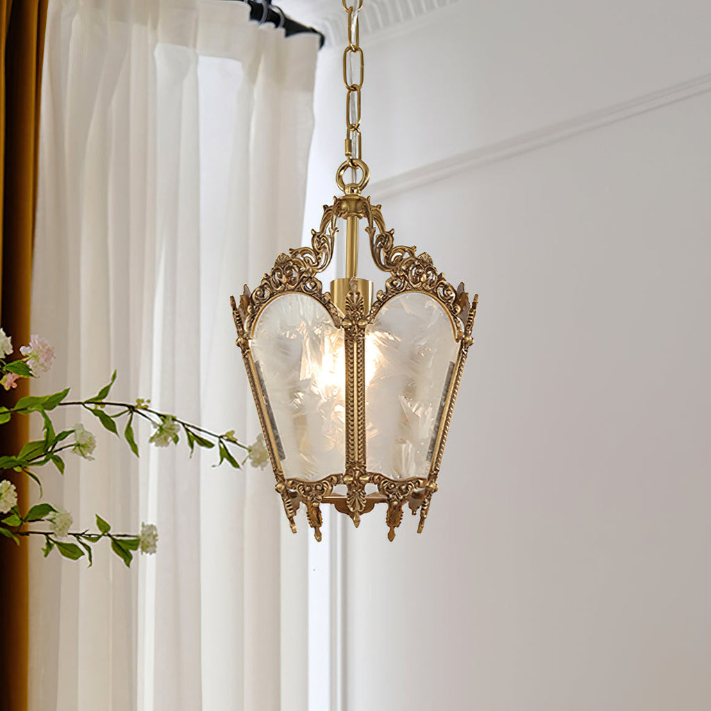 A brass Clérachic lantern pendant with frosted panels and a hanging chain, beside white curtains and a sprig of blossom.