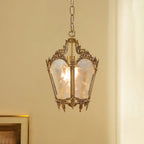A lit Clérachic lantern pendant with carved brass scrollwork hangs against a warm cream wall, beside a gilt picture frame.