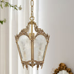 Close view of a Clérachic lantern pendant with an ornate brass crown and frosted glass, hanging by sheer white curtains.