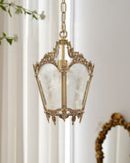 A Clérachic lantern pendant hangs in front of sheer curtains, with the edge of a gilt oval mirror at the lower right.