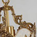Close view of the carved brass scrolls and central stem at the top of this Clérachic lantern pendant, with frosted glass below.