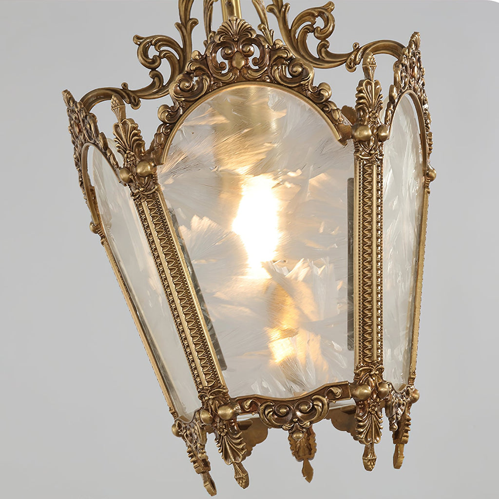 Close view of a lit Clérachic lantern pendant, with its frosted glass panels, patterned brass edging and small pendant drops at the base.