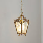 A lit Clérachic lantern pendant on a pale grey backdrop, its frosted panels glowing and its brass crown finely detailed.