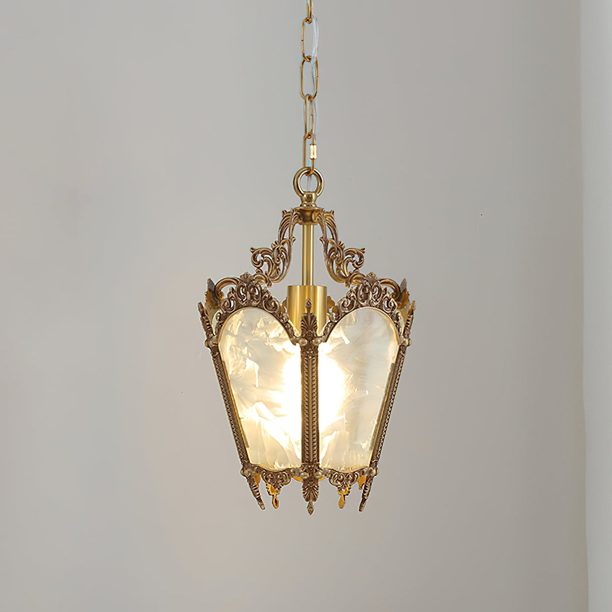 A lit Clérachic lantern pendant on a pale grey backdrop, its frosted panels glowing and its brass crown finely detailed.