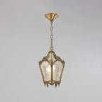A Clérachic lantern pendant with a darker, aged brass finish hangs from a round brass canopy on a pale grey backdrop.