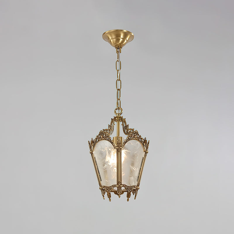 A Clérachic lantern pendant with a darker, aged brass finish hangs from a round brass canopy on a pale grey backdrop.