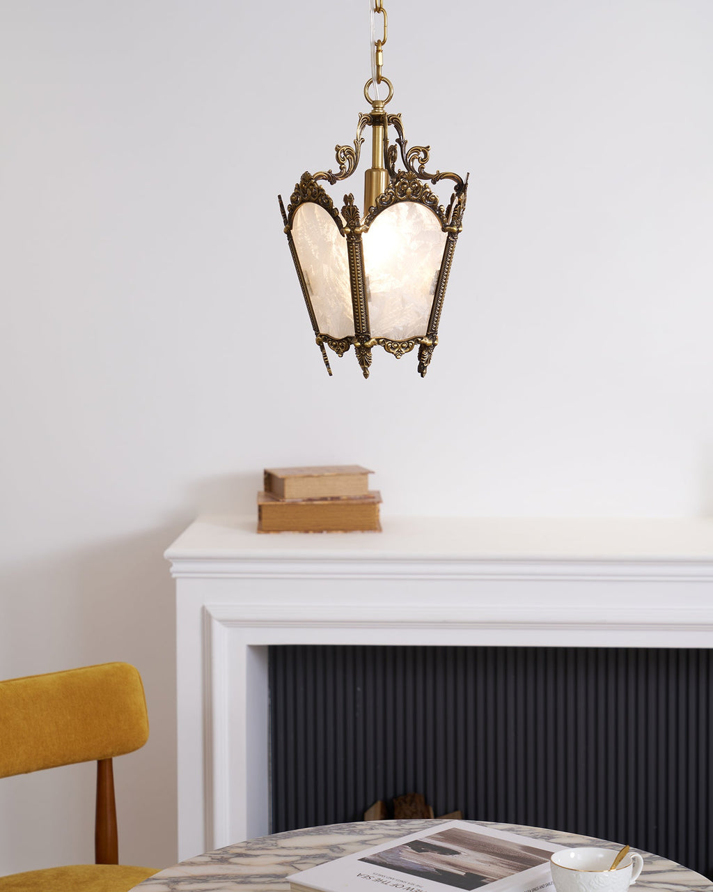 A Clérachic lantern pendant with frosted panels hangs above a white mantel with a stack of books and a mustard chair.