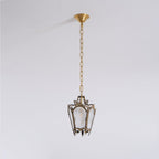 Seen from further away, a Clérachic lantern pendant hangs from a long chain and a brass canopy on a pale grey backdrop.