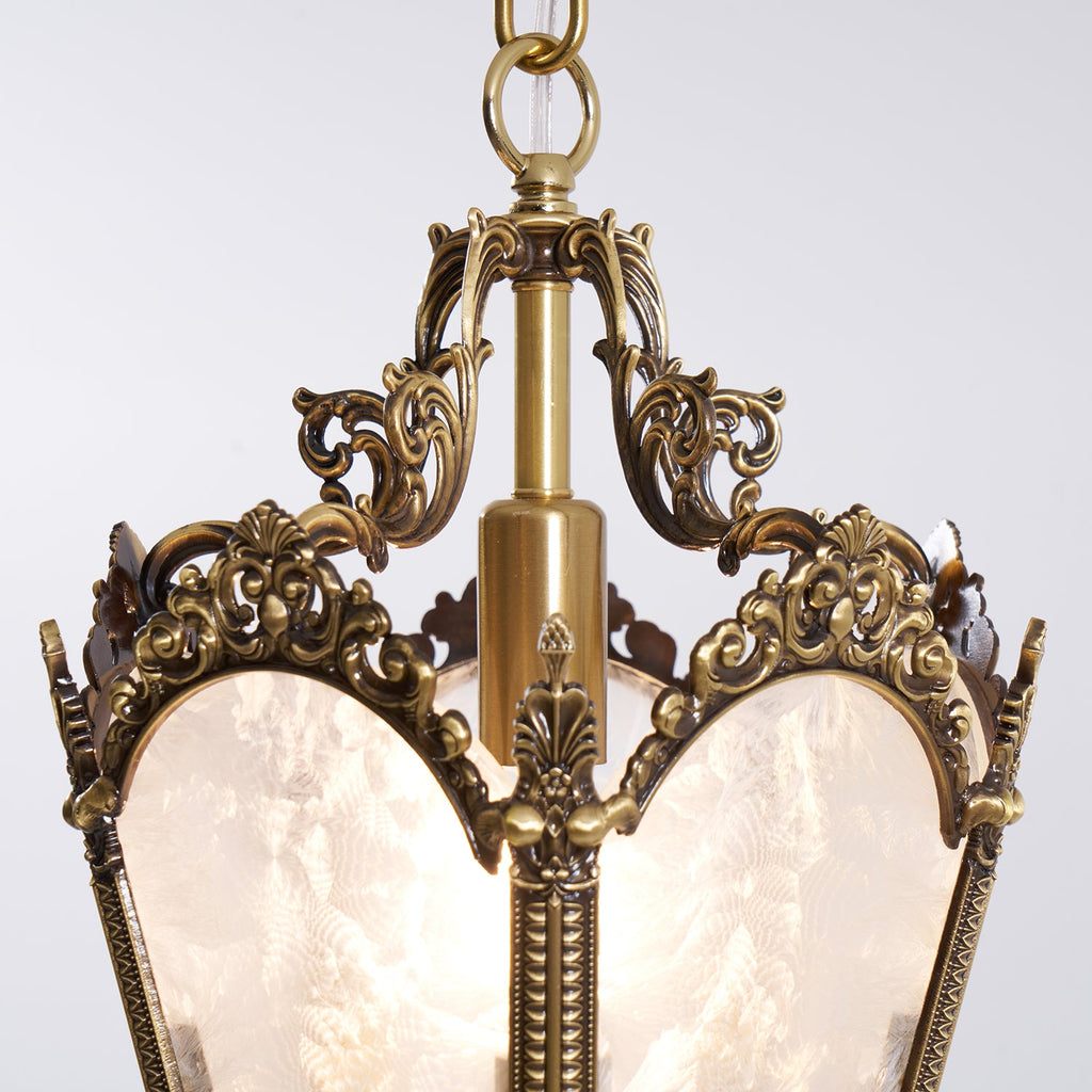 Close view of the carved brass crown and central column at the top of this Clérachic lantern pendant, above frosted glass panels.