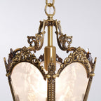 Close view of the carved brass crown and central column at the top of this Clérachic lantern pendant, above frosted glass panels.