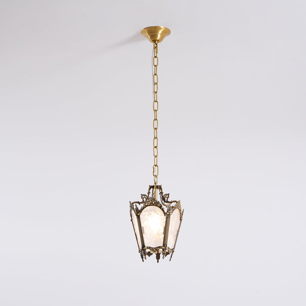 An unlit Clérachic lantern pendant with an aged brass frame hangs from a brass canopy against a plain pale wall.
