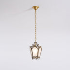An unlit Clérachic lantern pendant with an aged brass frame hangs from a brass canopy against a plain pale wall.