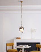 A Clérachic lantern pendant hangs from a long chain in a white room, above a marble table, a mantel and two mustard chairs.