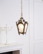 A lit Clérachic lantern pendant hangs beside a white candelabra and a panelled wall, with a mantel below.