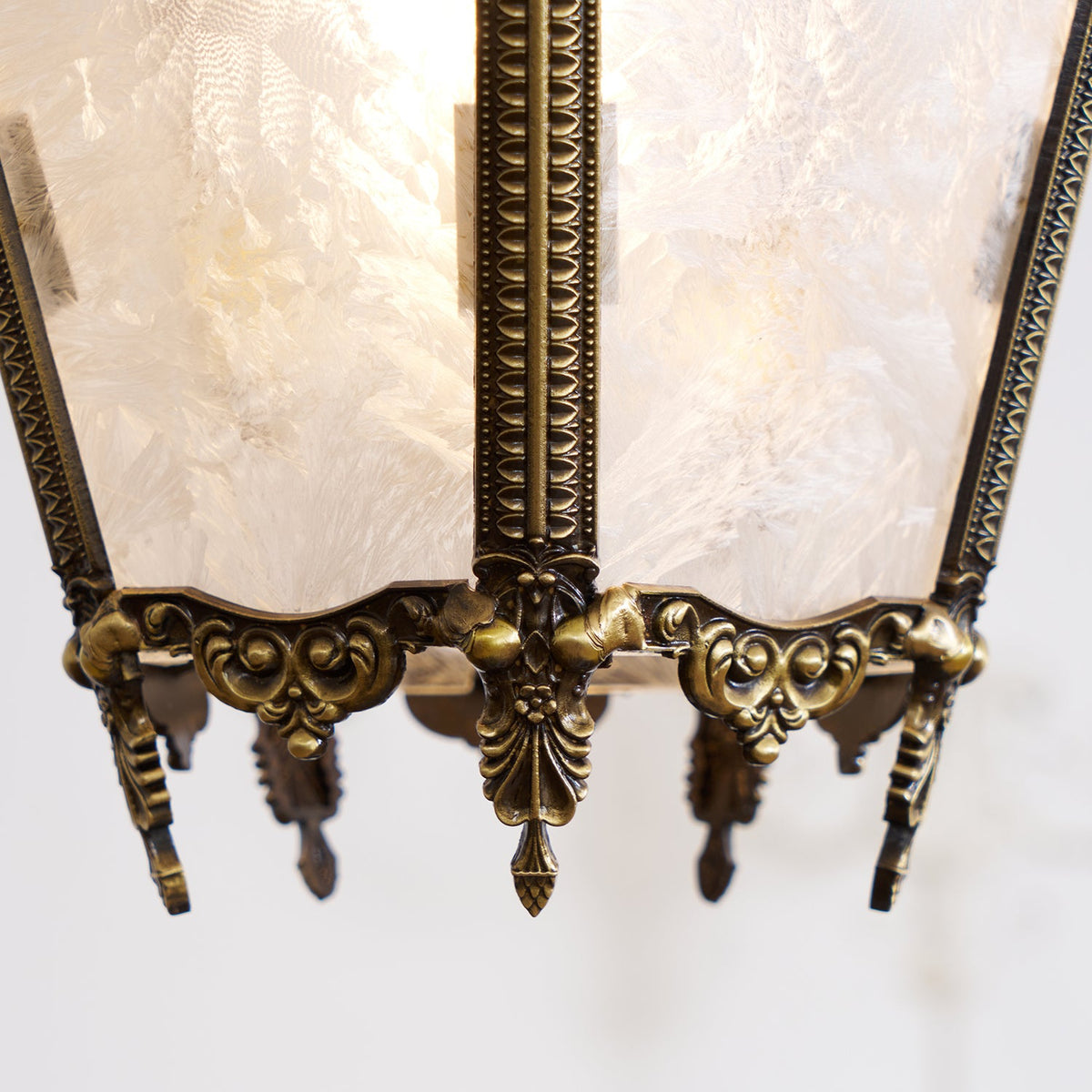 Close view of the base of this Clérachic lantern pendant, with a carved brass finial and frosted glass panels showing a feathery frost pattern.