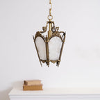 A Clérachic lantern pendant with white frosted panels and a darker brass frame hangs above a white mantel with two books.