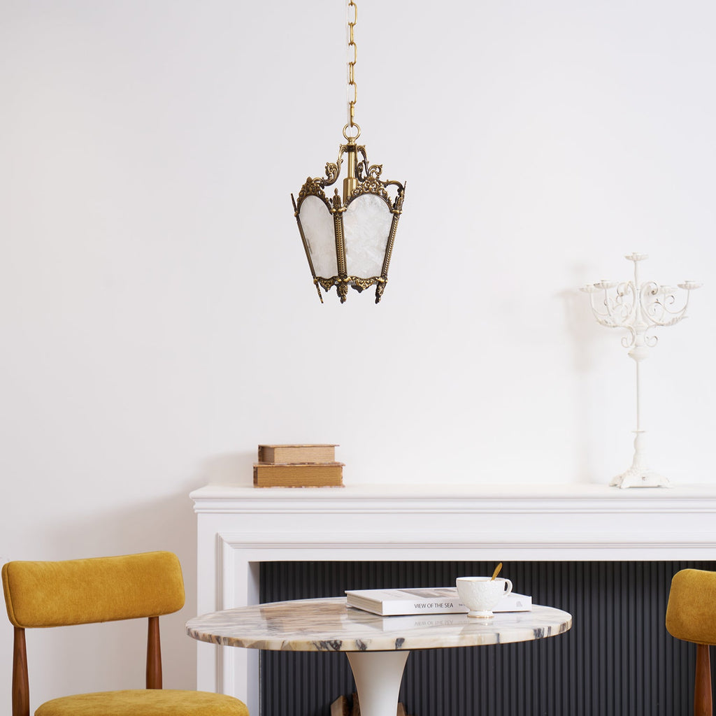 A Clérachic lantern pendant hangs above a marble round table and mustard chairs, with a white candelabra on the mantel.