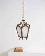 A Clérachic lantern pendant hangs on a chain above a white mantel with two books, against a plain white wall.