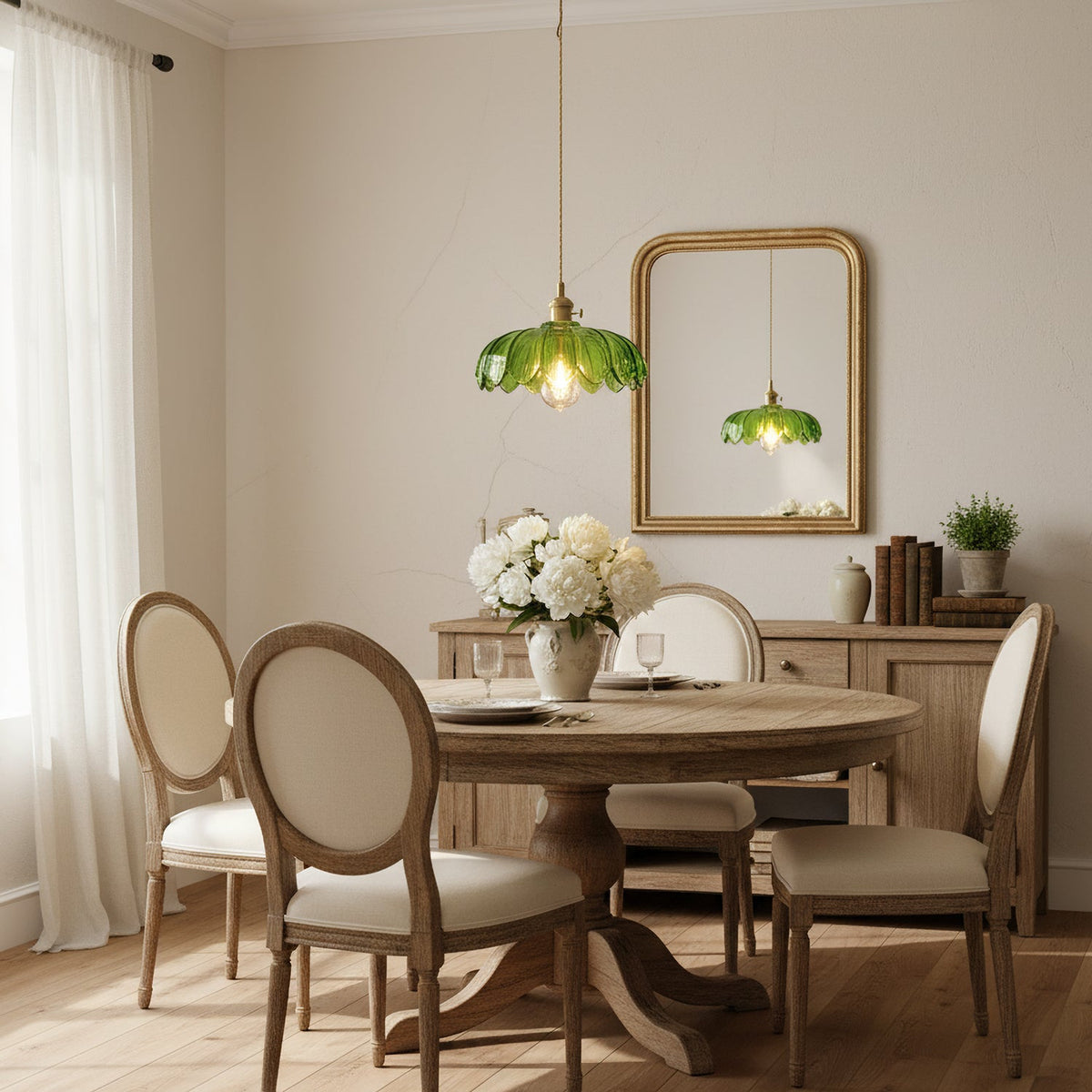 A green petal-edged Clérachic pendant hangs over a round wooden table with cane-backed chairs, beside a gold-framed mirror.