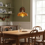 Lit Clérachic pendant in amber glass above a long wooden kitchen table with bentwood chairs, in front of an olive green wall.