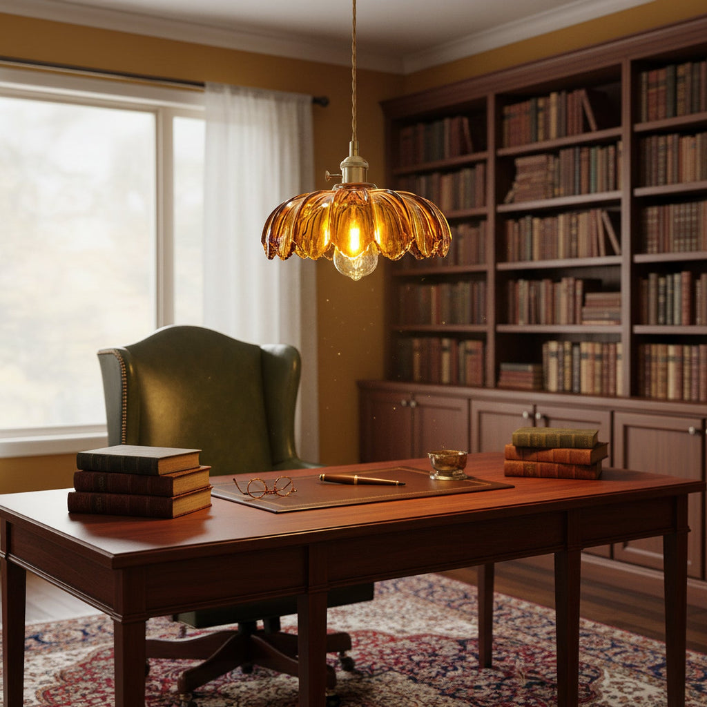 An amber glass Clérachic pendant glows above a mahogany desk in a study, with a tall bookcase and a green wingback chair behind.