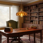 An amber glass Clérachic pendant glows above a mahogany desk in a study, with a tall bookcase and a green wingback chair behind.