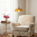 A petal-shaped amber Clérachic pendant glows above a floral armchair and a small white side table with pink flowers.