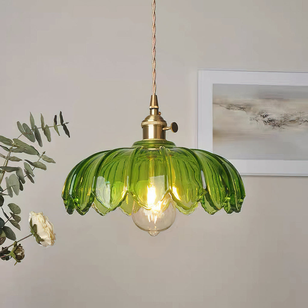 Lit green glass Clérachic pendant with a brass switch fitting, in front of a framed grey print and a sprig of eucalyptus.