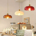 Three Clérachic pendants in amber, white and red glass hang at different heights above a café counter with glass jars.