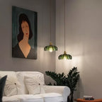 Two small green glass Clérachic pendants hang at different heights near a portrait painting and a white sofa.