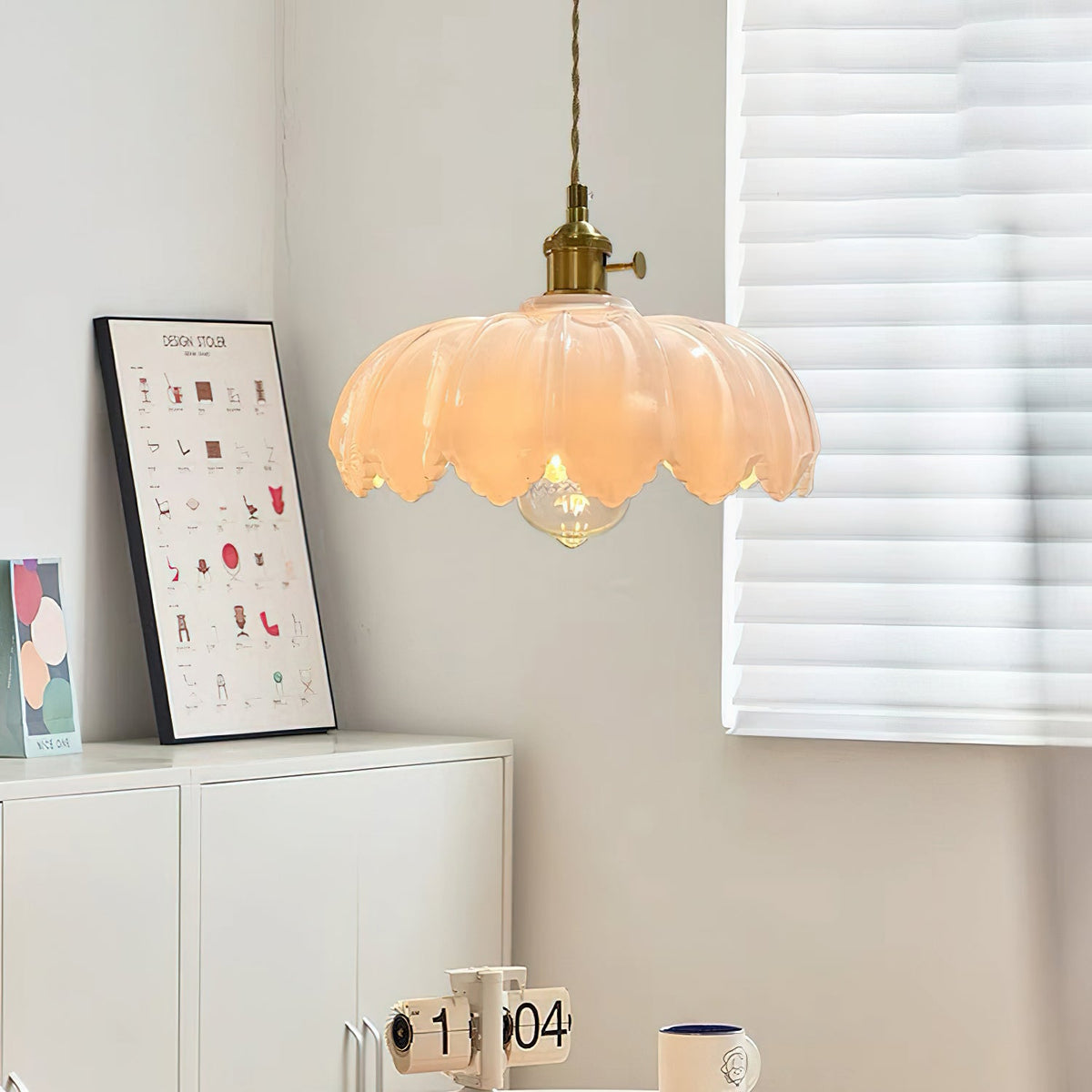 A Clérachic pendant with a pale pink-white glass shade and a brass fitting, near a window blind and a white cabinet.