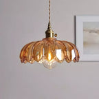A pale amber-pink Clérachic pendant with a petal-edged shade and a lit bulb, in front of a framed grey print.