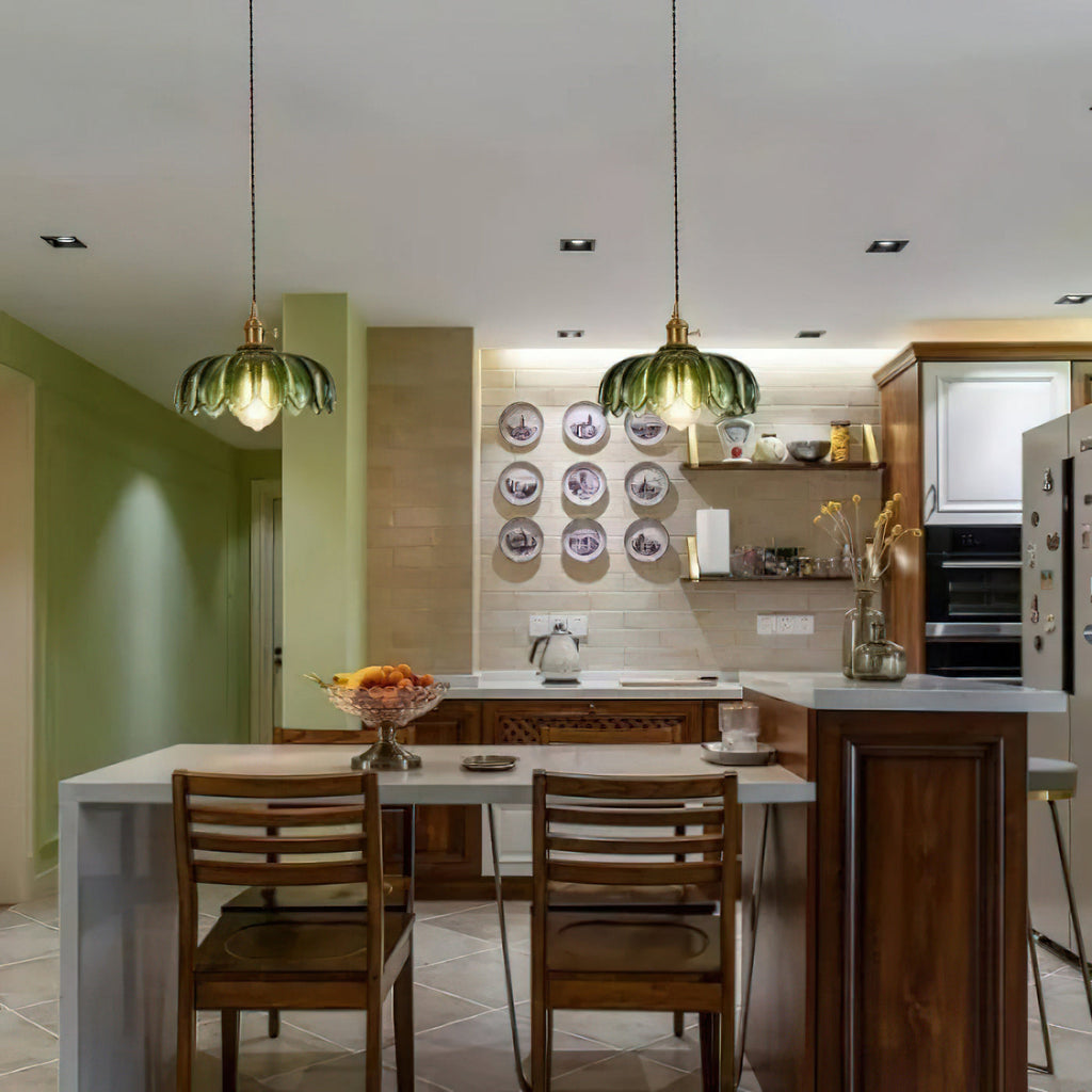 Two green glass Clérachic pendants hang in a kitchen with a dark wood table, wooden chairs and green walls.