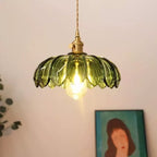 Lit green glass Clérachic pendant with a warm bulb, seen from slightly below, with a framed portrait at the bottom of the frame.