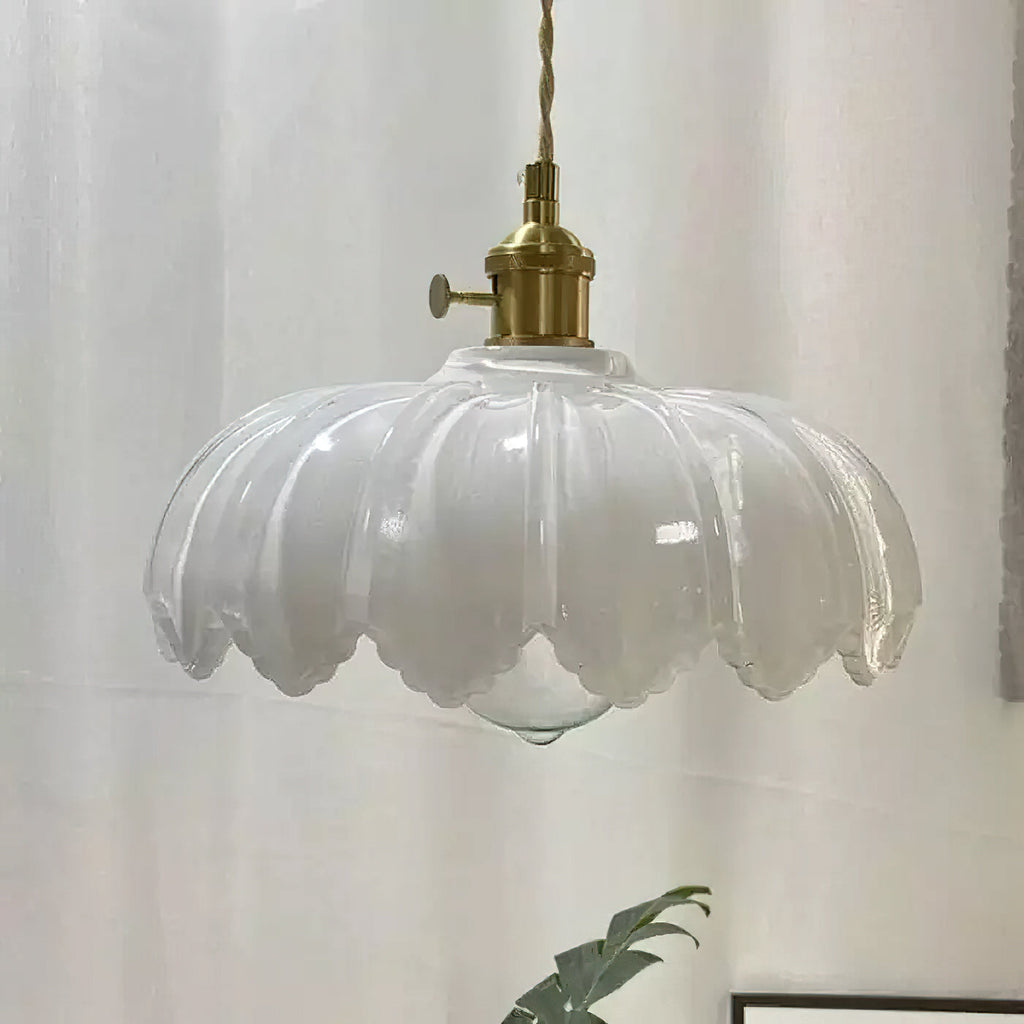 A white glass Clérachic pendant with a ribbed, petal-edged shade and a brass switch fitting, in front of a white curtain.