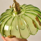 Close view inside a green glass Clérachic shade, held in one hand, showing its ribs, brass socket and filament bulb.