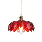 Red glass Clérachic pendant with a brass fitting and a lit bulb, on a plain white backdrop.