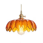 Amber glass Clérachic pendant with a petal-edged shade and a lit bulb below, on a plain white backdrop.