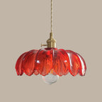 A red glass Clérachic pendant with a brass switch fitting and a clear bulb, on a taupe backdrop.