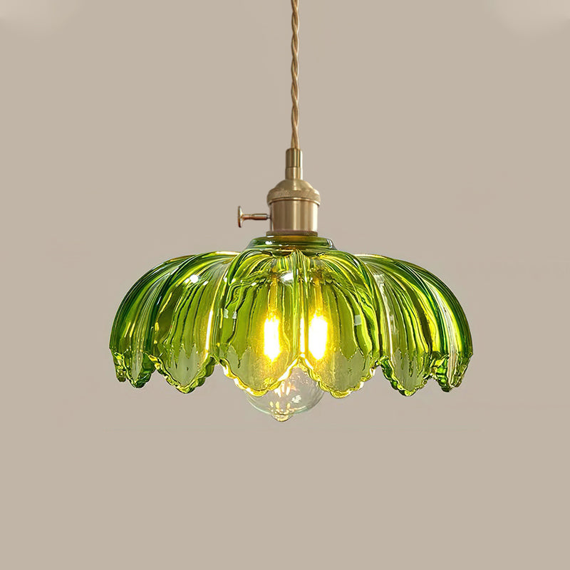 Green glass Clérachic pendant lit with a warm bulb, with a brass switch fitting and twisted cord, on a taupe backdrop.
